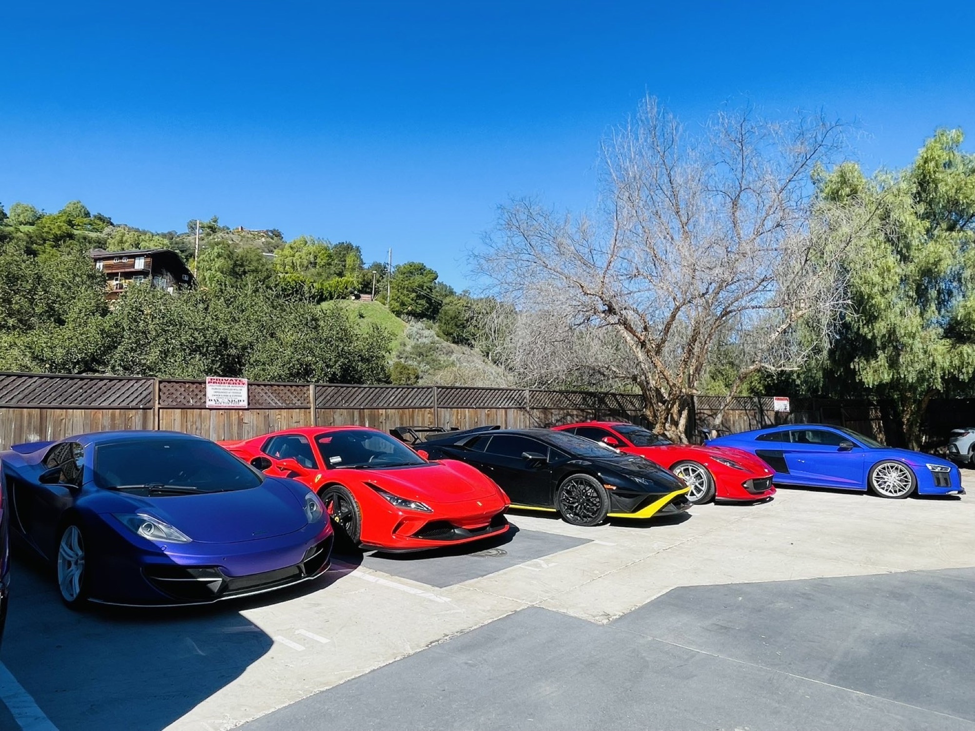 Five supercars lined up along a fence