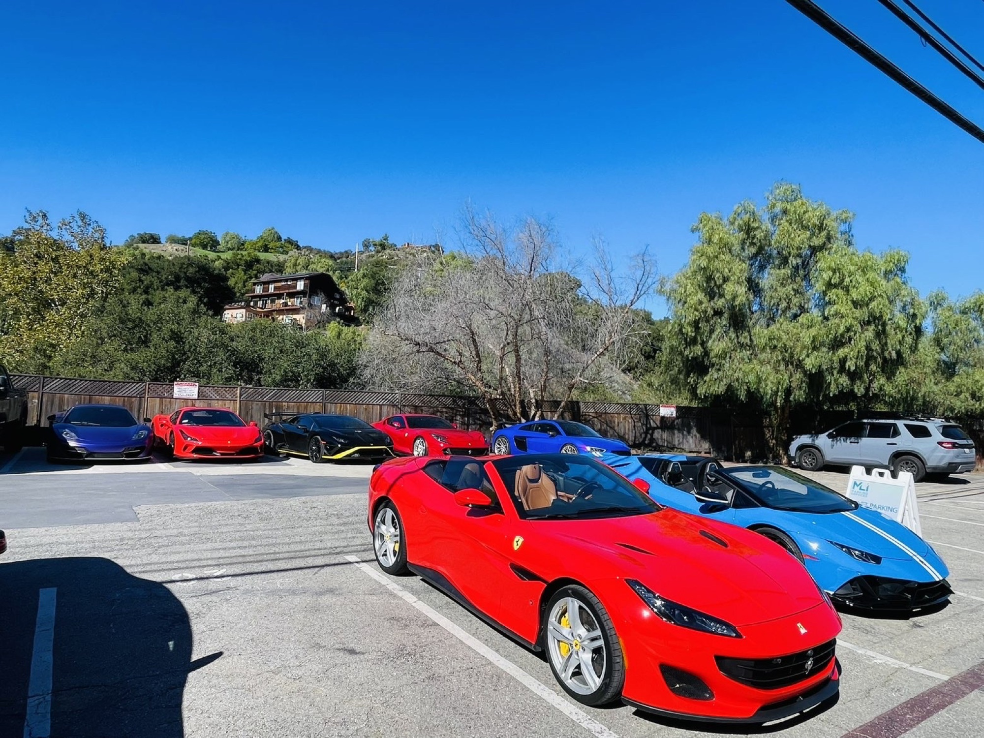 Two convertibles beside an MLI valet parking sign, with a row of supercars behind
